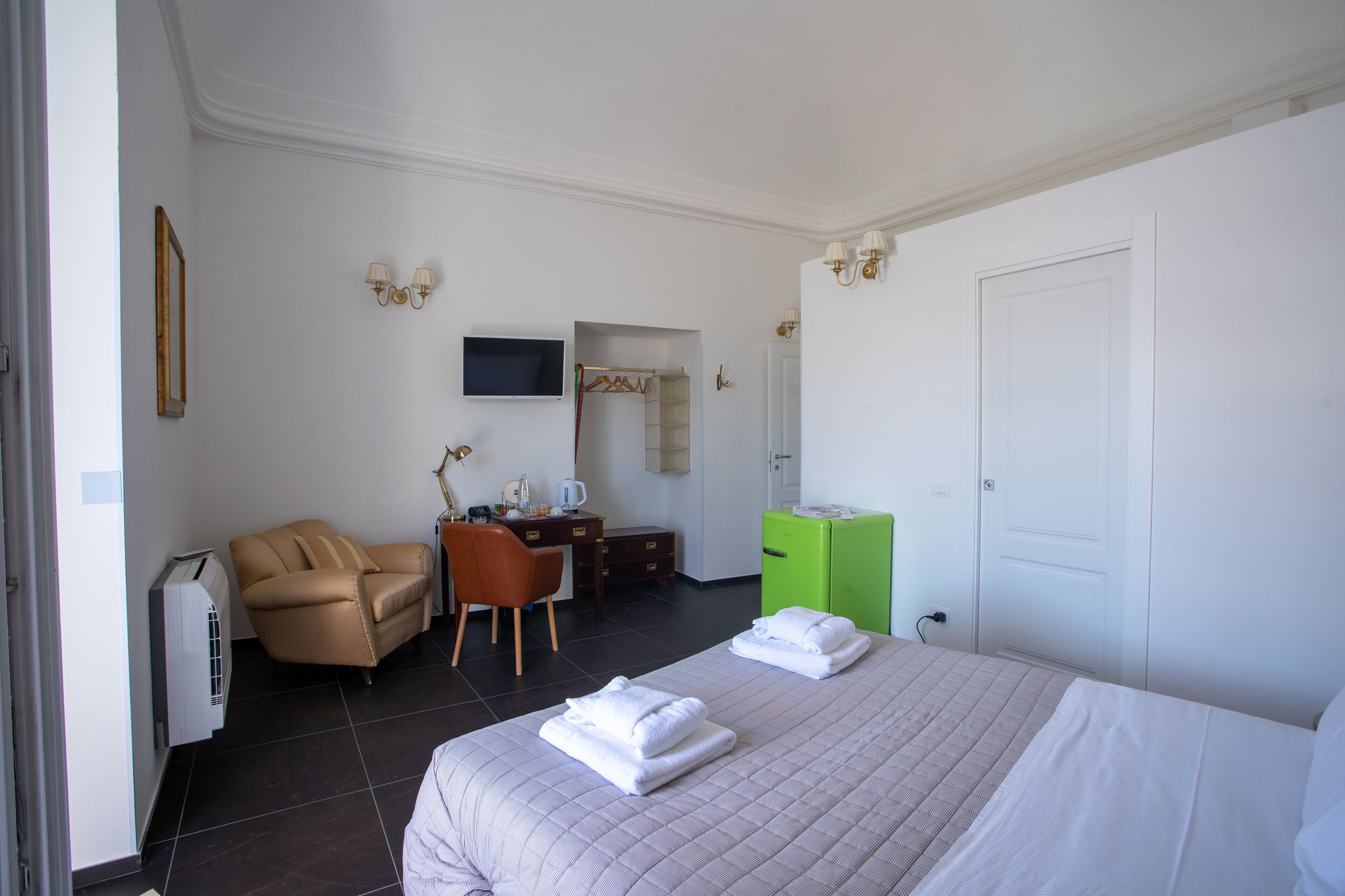 Una camera d'albergo con un letto, una sedia, una scrivania, una televisione e un armadio.