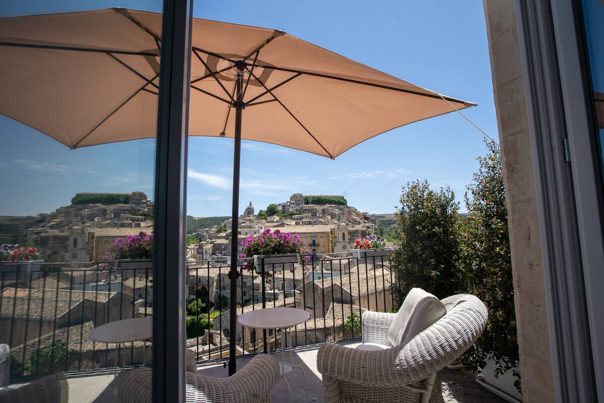A balcony with wicker furniture, a table, and a large umbrella.