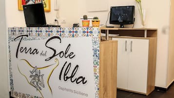 Ein Empfangstisch mit einem Schild, auf dem 'Terra del Sole Iblia' steht, und einer kleinen Kakteenpflanze darauf.