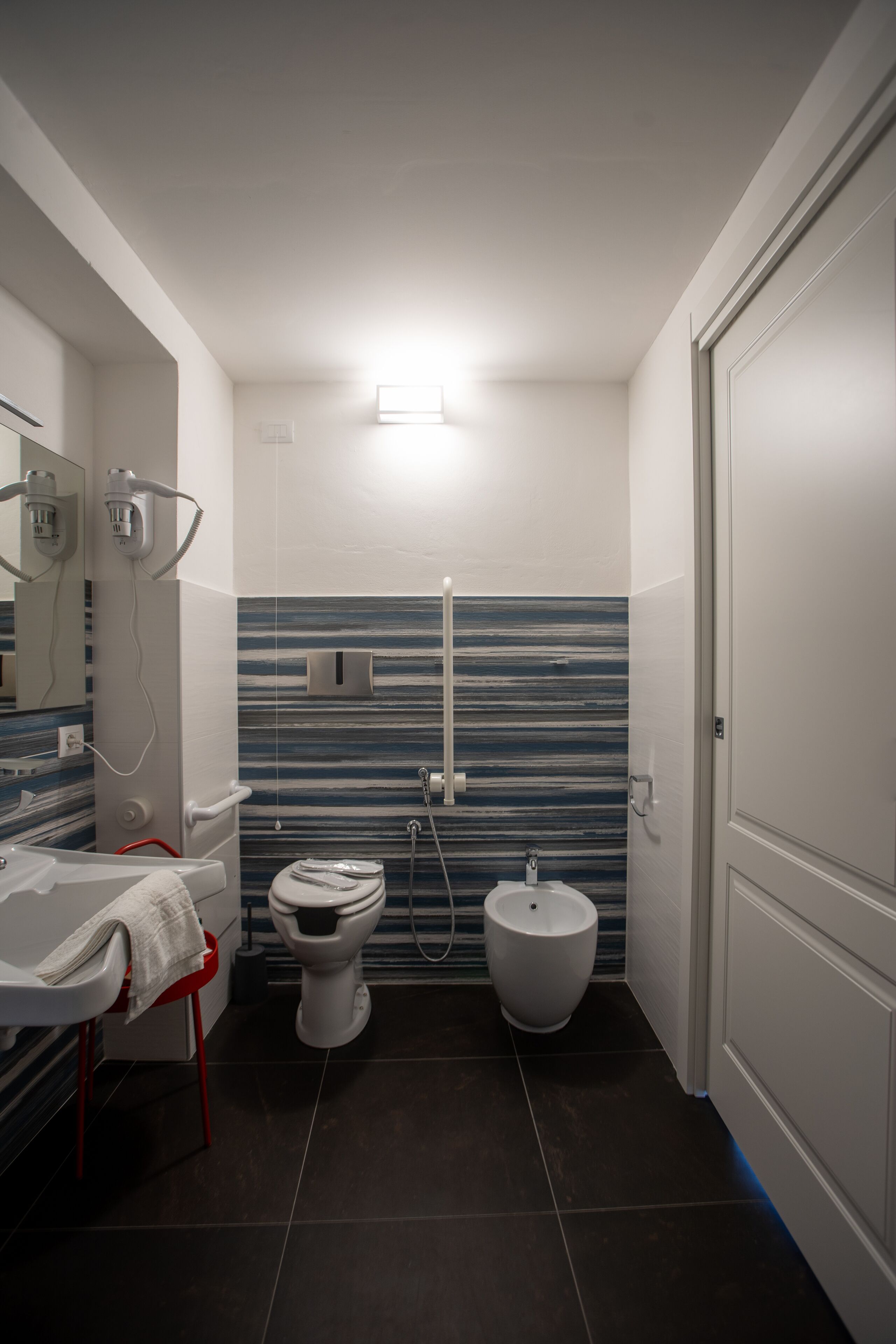 A compact bathroom with a toilet, bidet, and a sink with a towel rack.