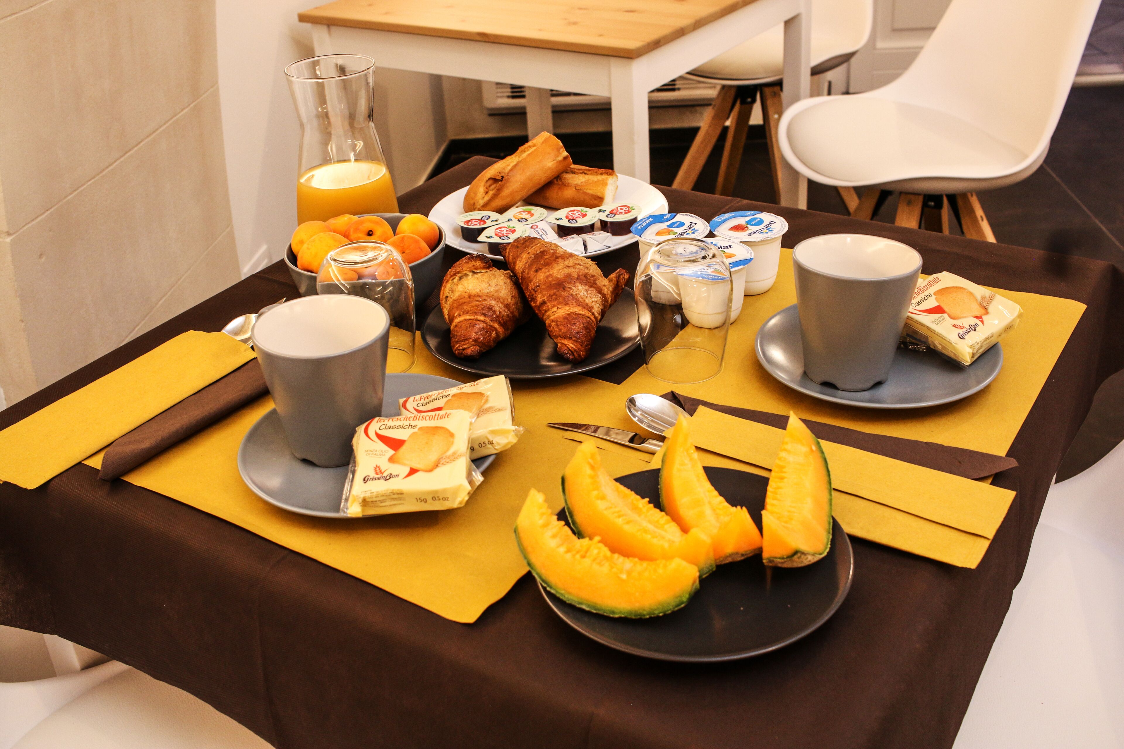 Une table de petit-déjeuner avec des croissants, du jus d’orange, du yaourt et du melon.