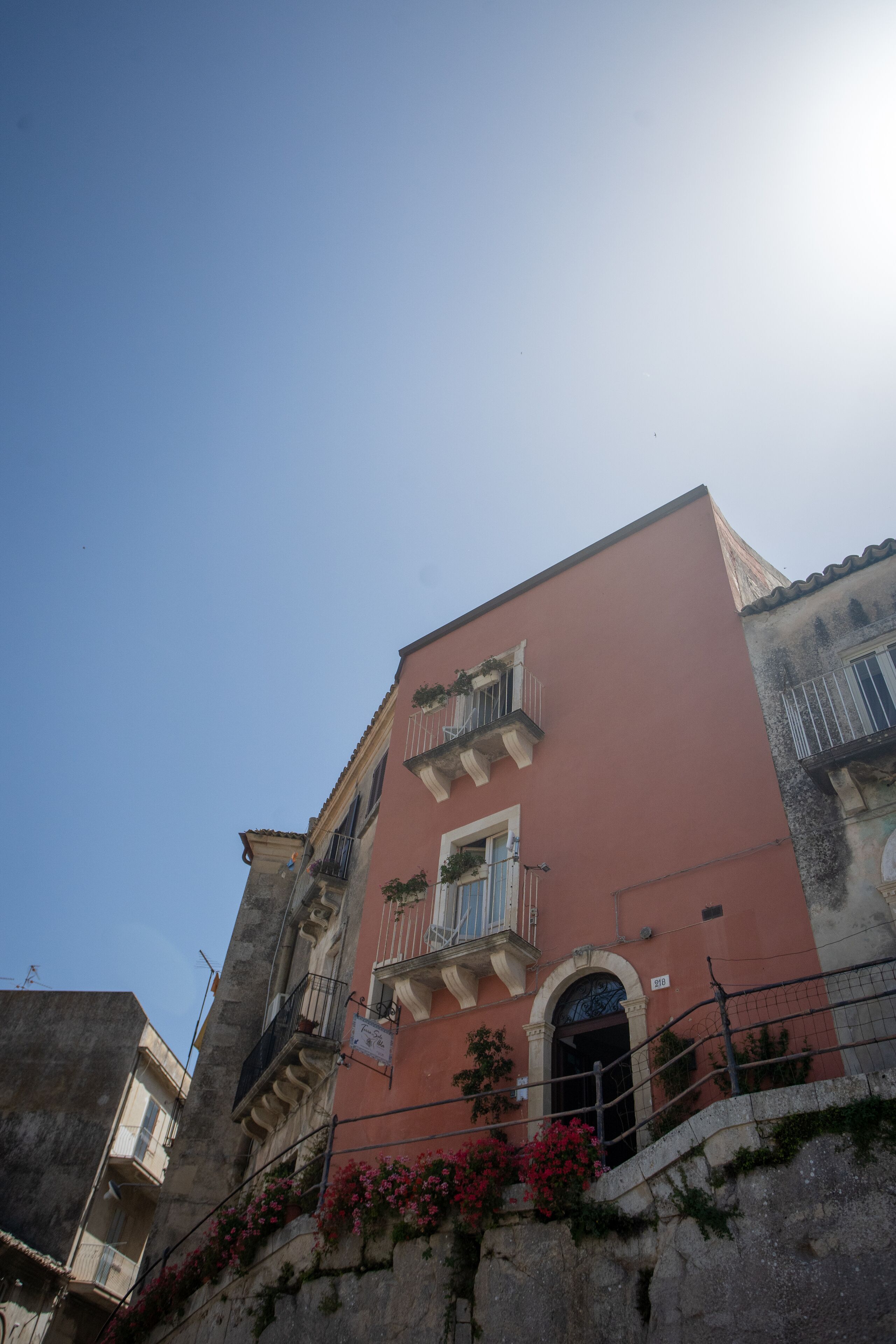 Un immeuble à plusieurs étages doté de balcons, un mur de pierre orné de fleurs et un ciel d’un bleu limpide.