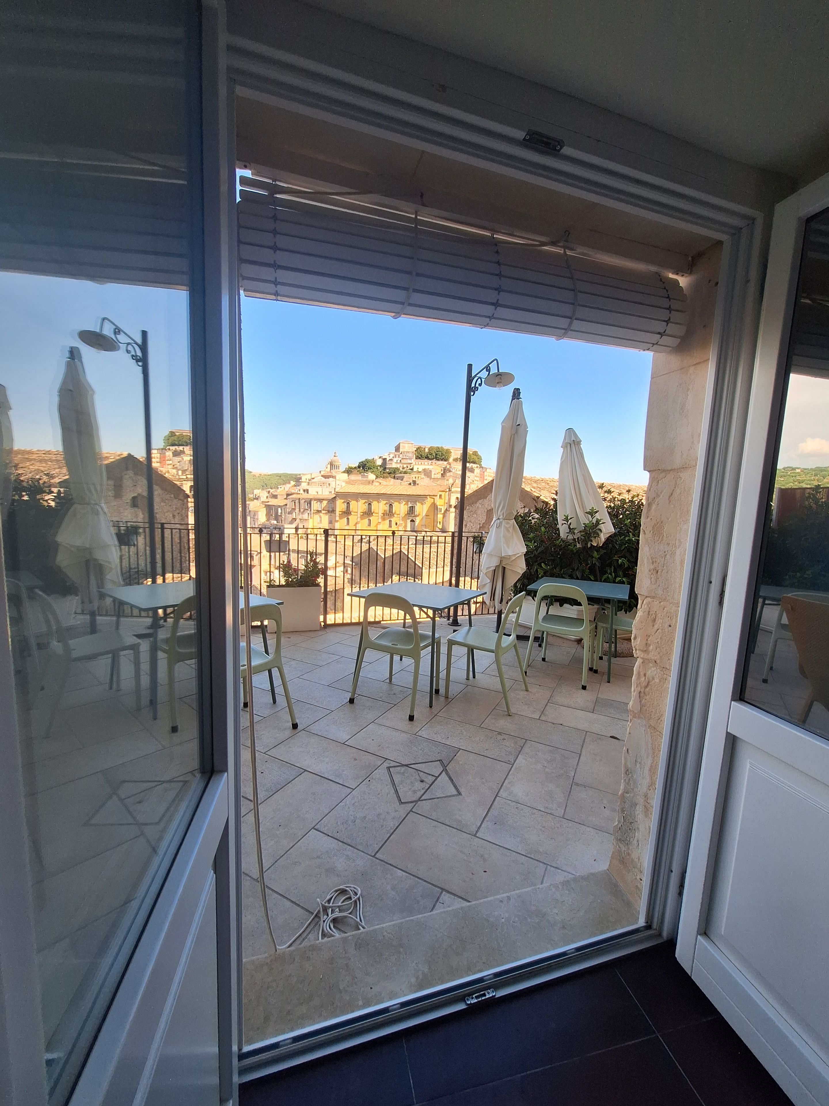 A balcony with outdoor furniture, a view of a cityscape, and a clear sky.