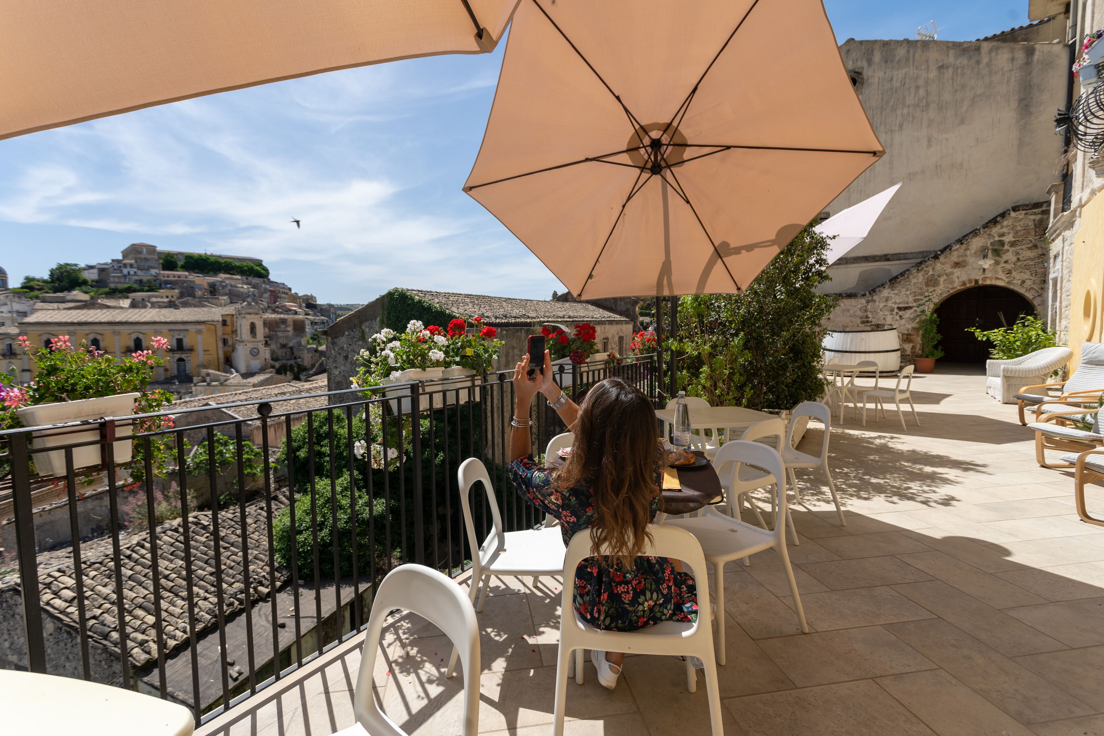 En terrasse med udendørs siddepladser, udsigt over byen og en stor parasol, der giver skygge.