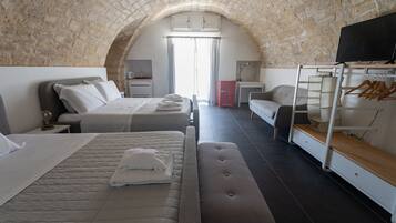 Habitación de hotel con techo de piedra abovedado, una cama con almohada y toalla doblada, un banco, un televisor, un armario y un perchero.