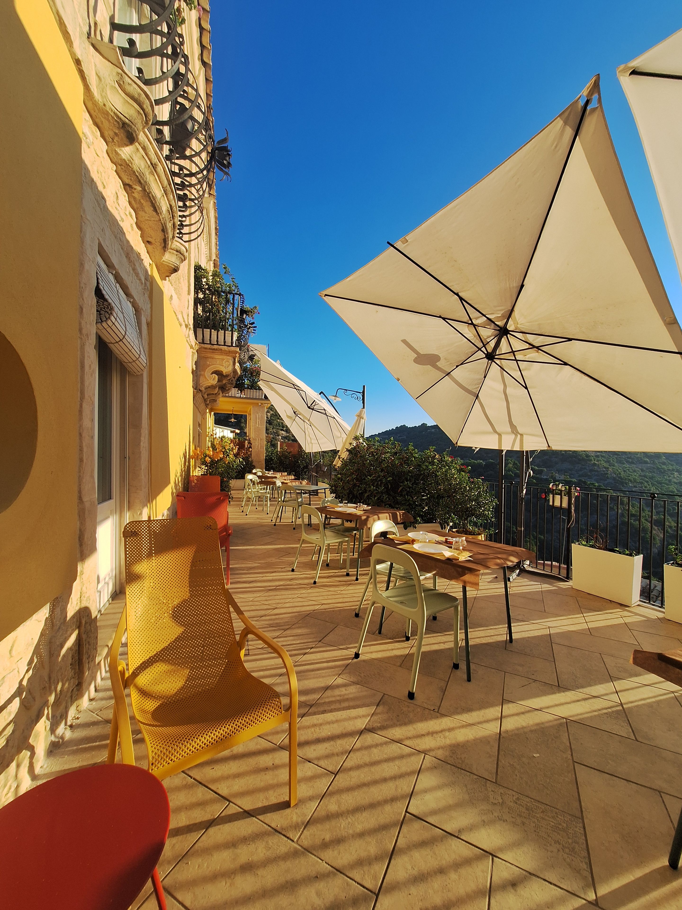 An outdoor seating area with tables and chairs, umbrellas, and a view of the landscape.
