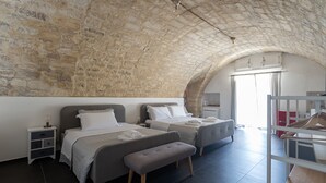 Un dormitorio con dos camas, un banco, un armario y techo de piedra.