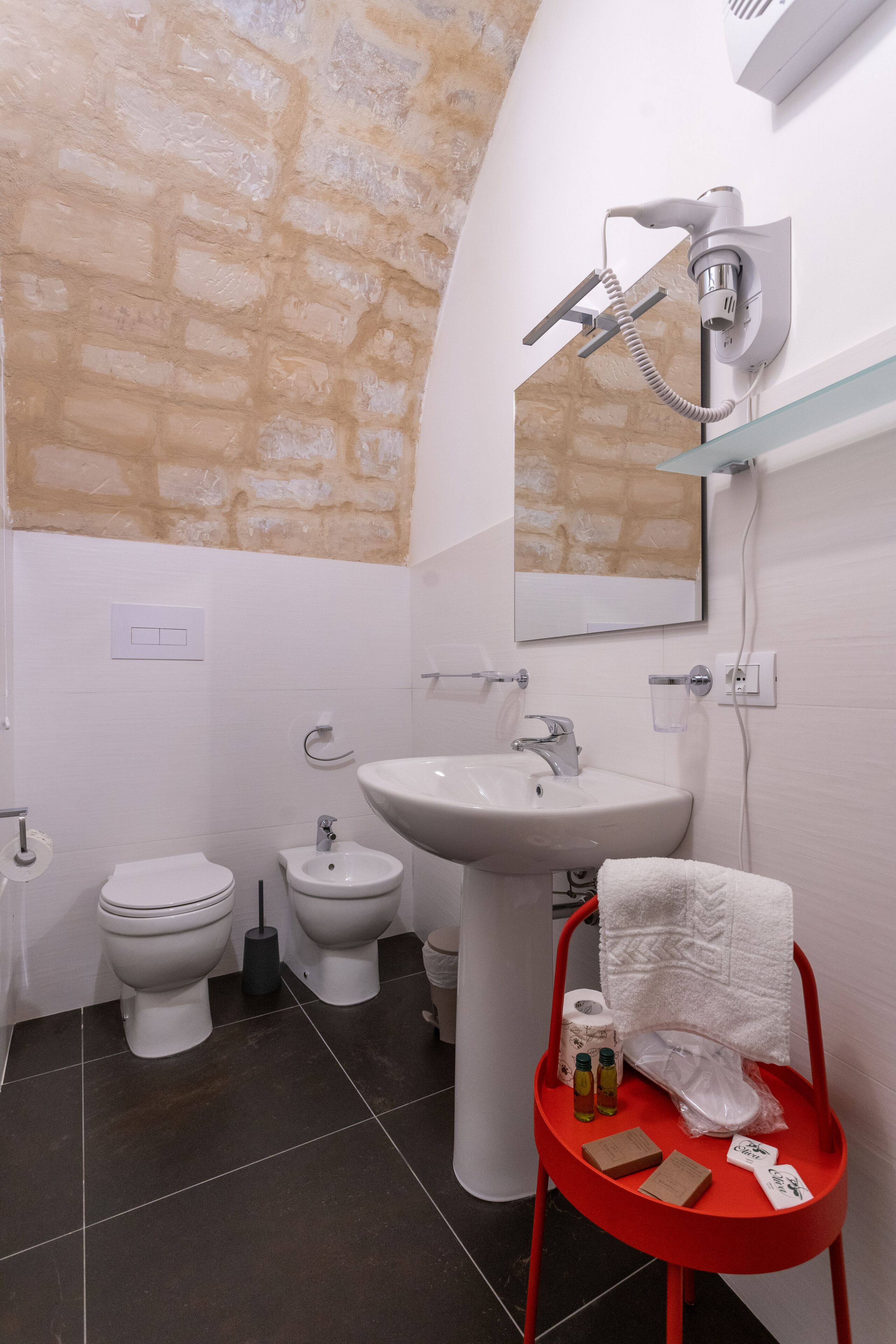 A bathroom with a white sink, a mirror, a towel rack, a red chair, and a shower head.