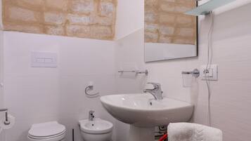 A bathroom with a white sink, a mirror, a towel rack, a red chair, and a shower head.