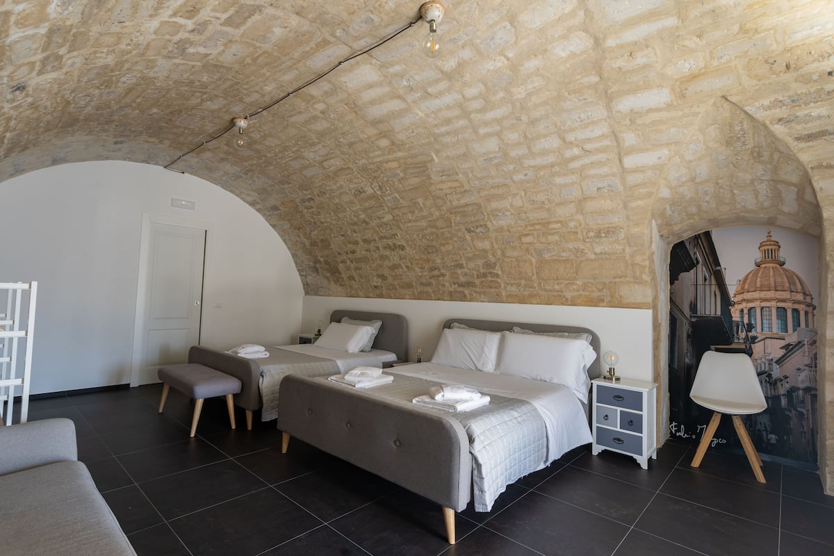 A bedroom with two beds, a white bench, a nightstand, and a mural on the wall.