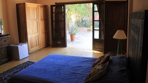 A bedroom with a bed, a wardrobe, a desk, and a view of an outdoor garden. - Maison Marocaine (Agadir)