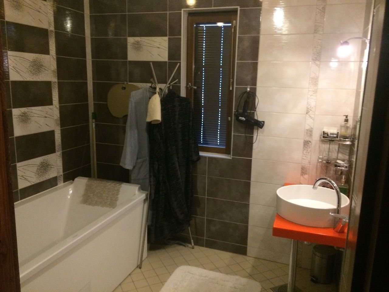 Un baño con bañera, lavamanos y ventana con persianas.
