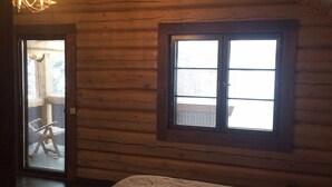 A log cabin bedroom with a bed, a chandelier, and a window. - Kalina Apartments (Savonlinna)