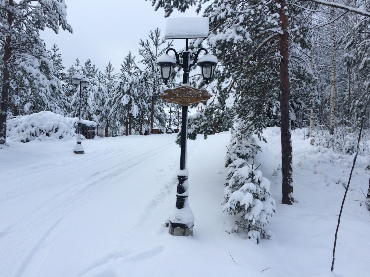 Lumipeitteinen katu, jossa on valaisinpylväs ja opastekyltti.