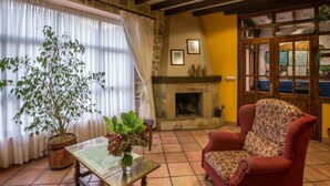 A cozy room with a fireplace, a red armchair, and a large window with curtains. - Hotel Villa de Cabrales (Cabrales)