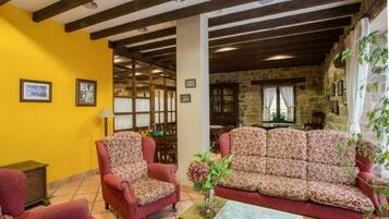 Una habitación acogedora con un sillón rojo, un sofá estampado y una zona de comedor con paredes de piedra y vigas de madera.