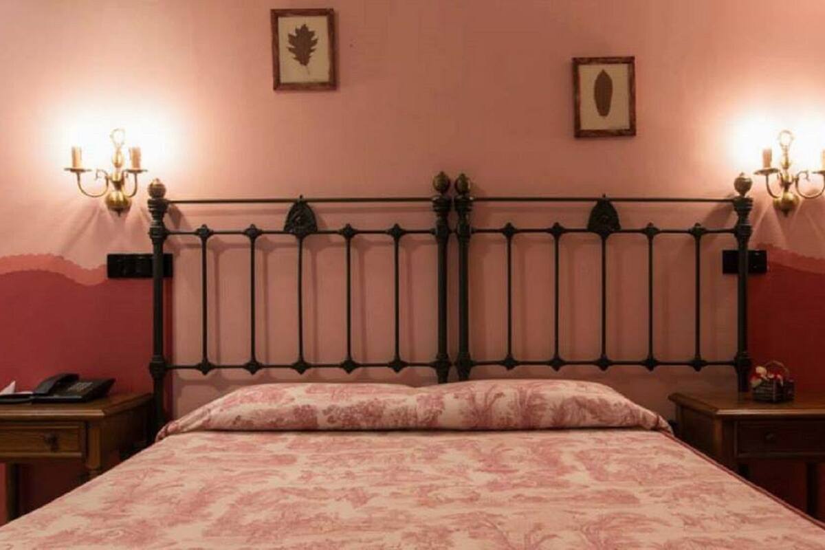 Una cama con cabecera de metal, dos mesitas de noche y apliques de pared.