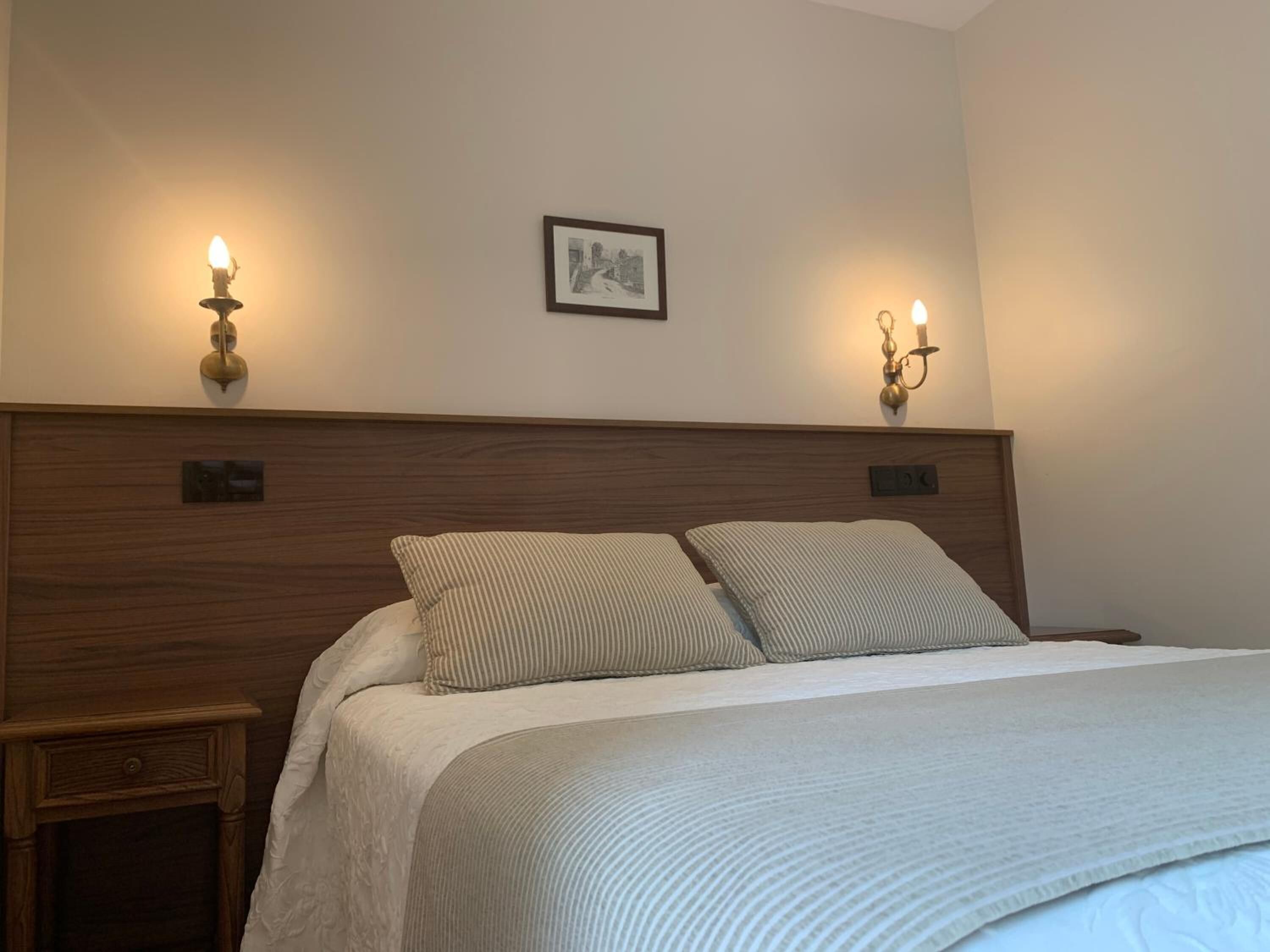 A neatly made bed with a wooden headboard, two bedside tables, and wall-mounted lamps.