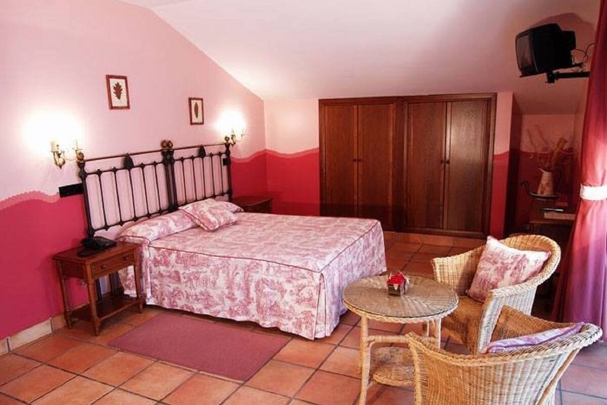 Un dormitorio con una cama, una mesita de noche, una silla de mimbre, una pequeña mesa y un armario.