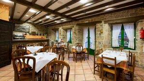 A restaurant with stone walls, wooden beams, and multiple tables with white tablecloths. - Hotel Villa de Cabrales (Cabrales)