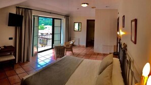 A hotel room with a bed, a desk, a chair, a TV, and a balcony with a view. - Hotel Villa de Cabrales (Cabrales)