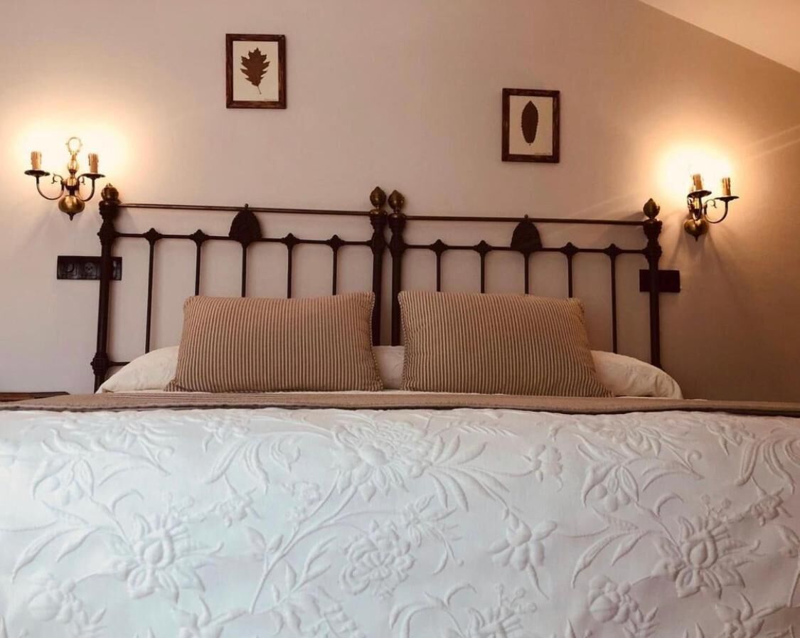 Un letto con copriletto a motivi floreali, due cuscini, una testiera in metallo scuro e applique con quadri a forma di foglia e ovale.