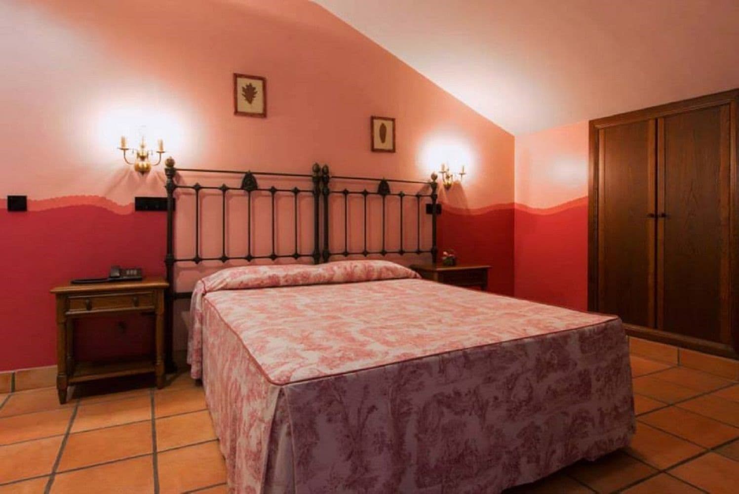 A bedroom with a bed, two bedside tables, a wardrobe, and two wall-mounted lamps.