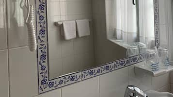 Un baño con secador de pelo montado en la pared, un espejo con marco decorativo, un perchero y un lavabo con grifo.