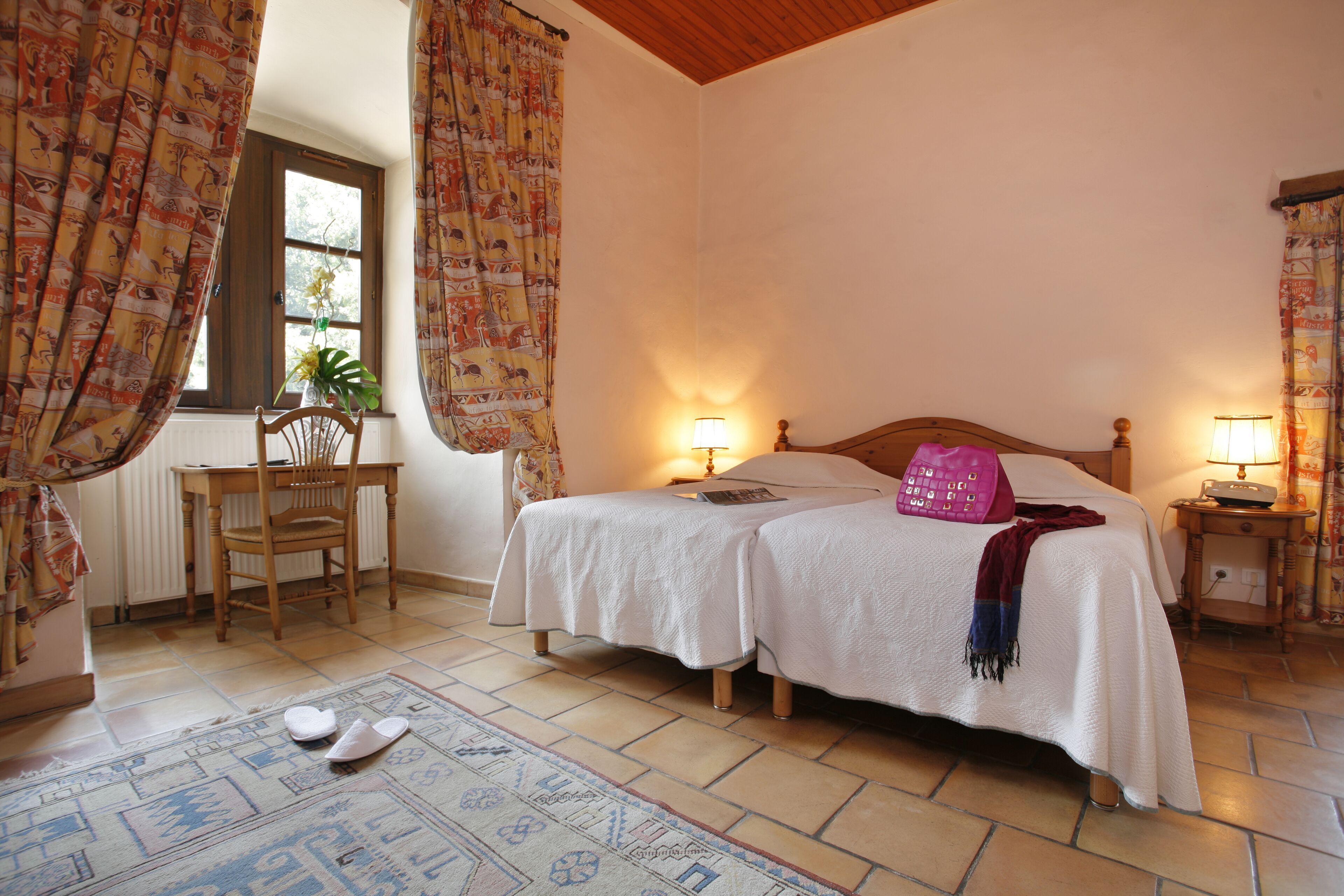 A bedroom with two beds, a wooden chair, a table, and a window with curtains.
