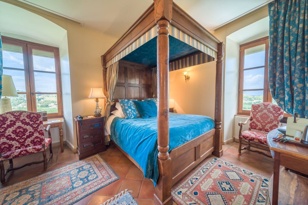 Un lit à baldaquin avec une couvre-lit bleue, deux tables de chevet, une chaise en bois et un tapis à motifs.