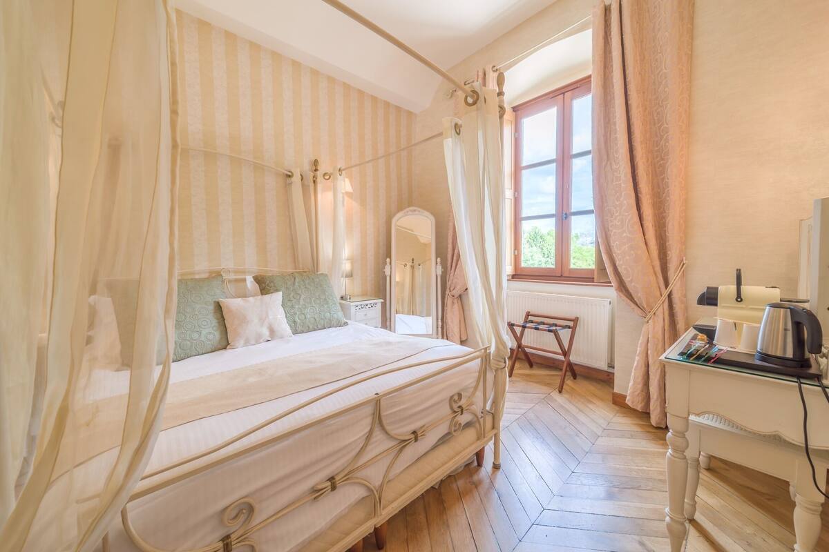Une chambre à coucher avec un lit à baldaquin, une table de chevet, une chaise et un bureau équipé d’une bouilloire.