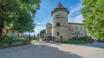 A historic stone building with a tower, surrounded by trees and a gravel driveway.