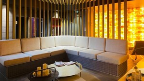 A modern lounge area with a curved sofa, a small round table with candles, and a decorative wall with vertical panels. - Château Chapeau Cornu (Vignieu)