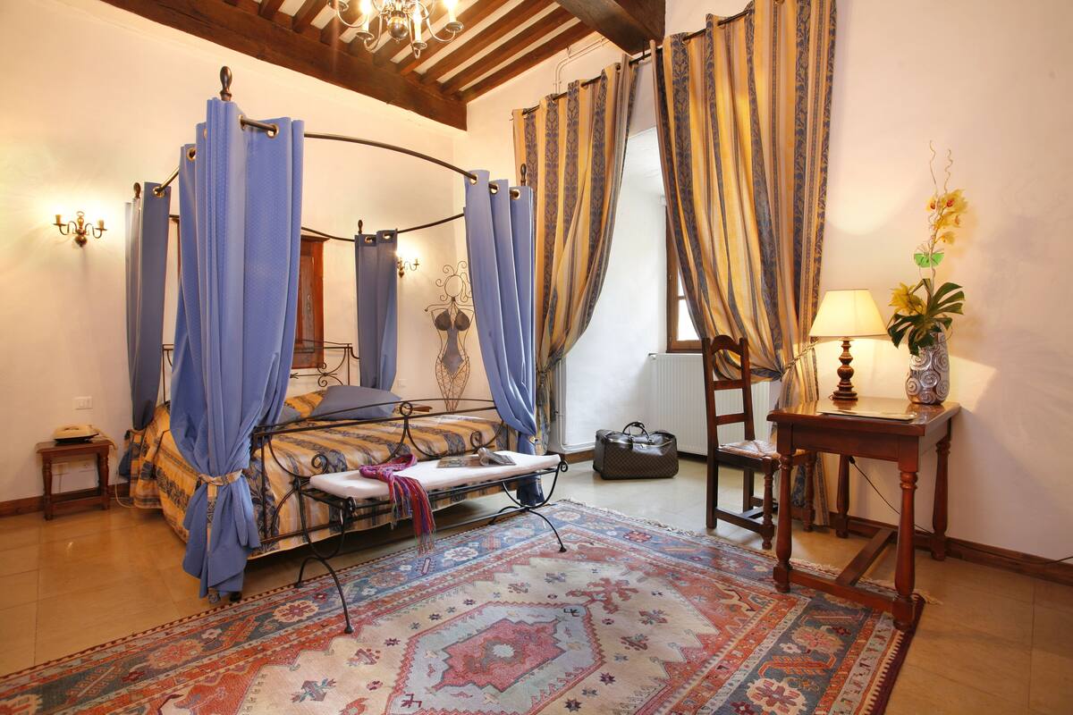 Une chambre à coucher avec un lit à baldaquin, un tapis à motifs, une table de chevet avec une lampe et des rideaux.