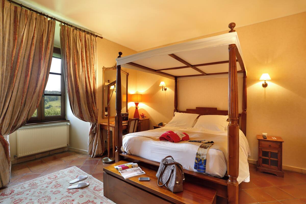 Un lit à baldaquin, une table de chevet avec une lampe, une commode et une fenêtre avec des rideaux.