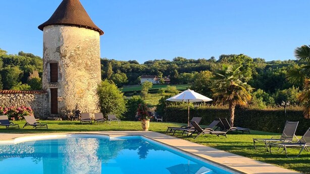 A swimming pool with lounge chairs and a stone tower. - Château Chapeau Cornu (Vignieu)