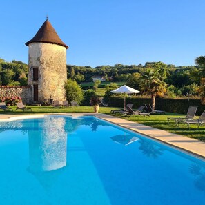 A swimming pool with lounge chairs and a stone tower. - Château Chapeau Cornu (Vignieu)