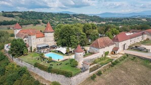 A historic castle with a swimming pool, surrounded by lush greenery and a stone wall. - Château Chapeau Cornu (Vignieu)