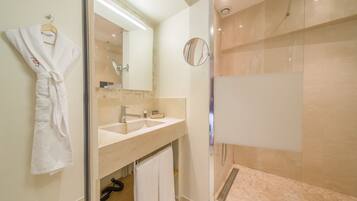 A modern bathroom with a glass-enclosed shower, a sink with a mirror, and a robe hanging on a rack.