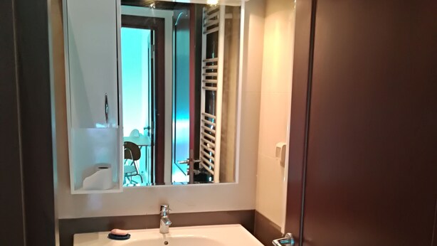 Ein Badezimmer mit einem weißen Waschbecken, einem Spiegel darüber und einer Tür rechts.