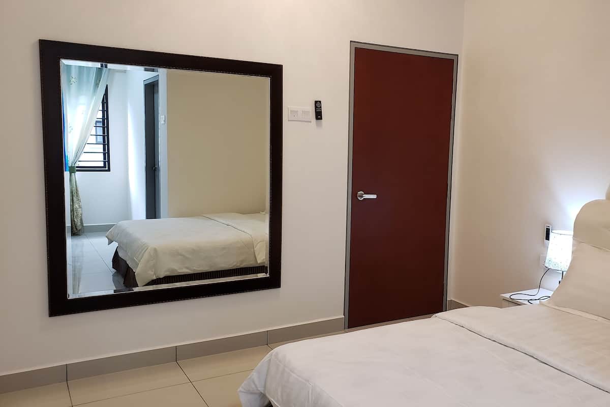 A bedroom with a large mirror, a bed, a door, and a light switch on the wall.