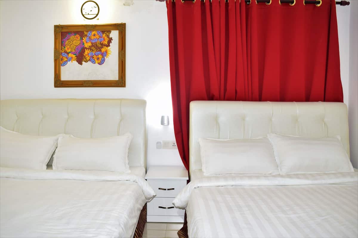 A hotel room with two beds, a red curtain, and a framed artwork on the wall.