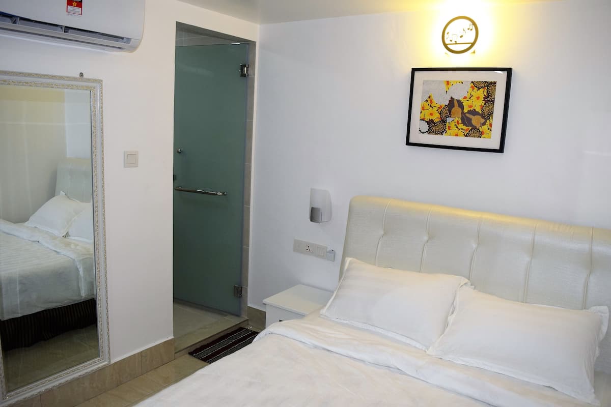 A hotel room with a bed, a bedside table, a mirror, a framed picture on the wall, and a door leading to a bathroom.