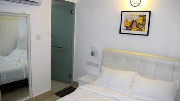 A hotel room with a bed, a bedside table, a mirror, a framed picture on the wall, and a door leading to a bathroom.
