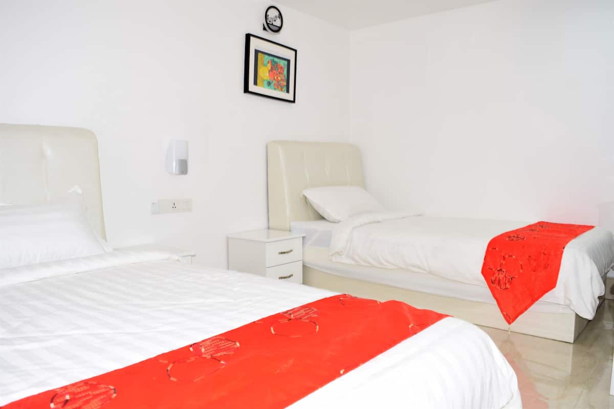 A hotel room with two beds, a nightstand, a wall clock, and a framed picture.
