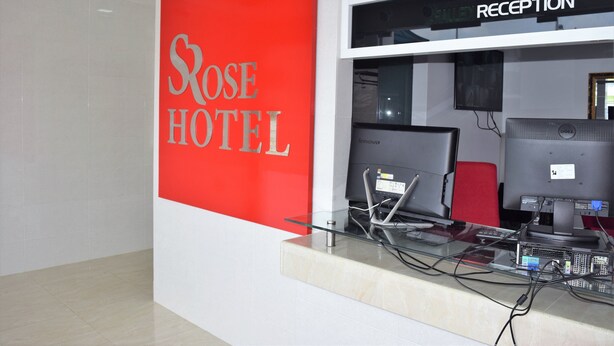 Un comptoir d'accueil avec une enseigne rouge sur laquelle on peut lire « Rose Hotel » et une autre enseigne, plus petite, au-dessus, indiquant « Réception ».