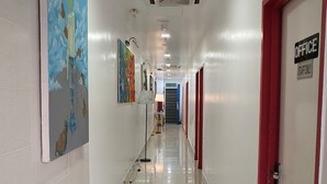 Un couloir propre et bien éclairé, avec un sol carrelé, des portes à cadre rouge et des œuvres d’art accrochées aux murs.