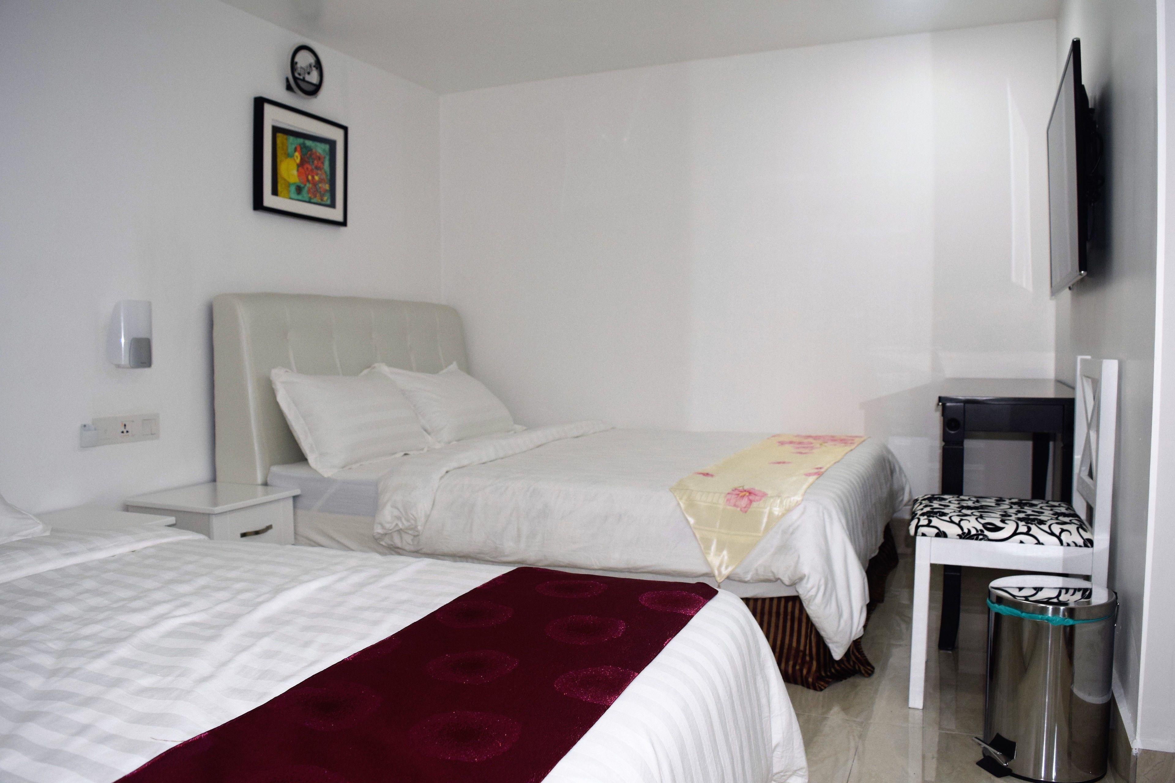 Habitació d'hotel amb dos llits, una taula de nit, una cadira, un safataire i un televisor fixat a la paret.