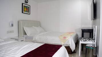 Habitació d'hotel amb dos llits, una taula de nit, una cadira, un safataire i un televisor fixat a la paret.
