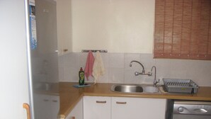 A compact kitchen with a sink, a dish rack, and a refrigerator.